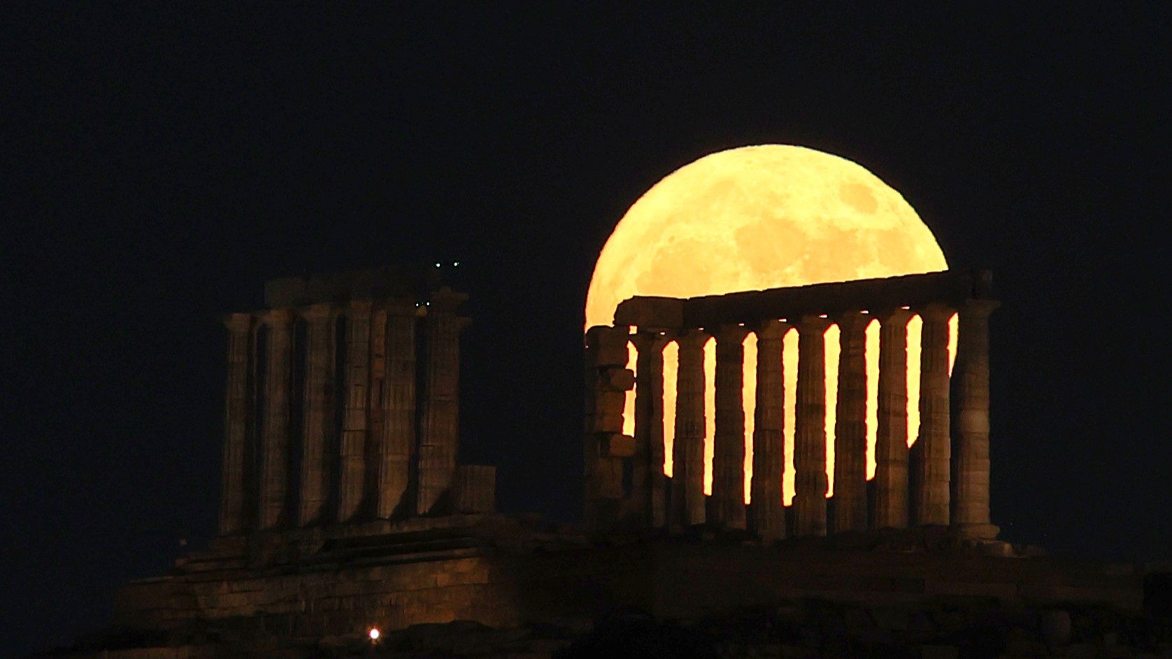 large yellow moon appears behind stone columns.