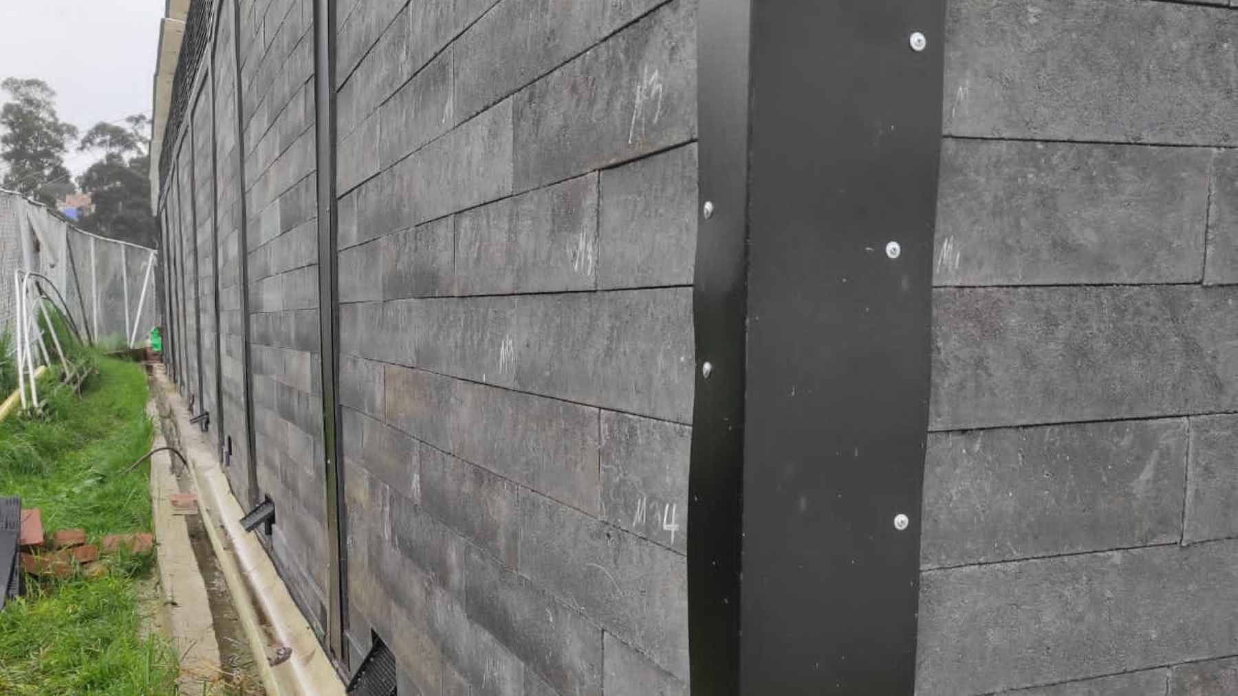 A construction worker assembling a modular wall using interlocking, bright-colored bricks made from 100% recycled plastic waste.
