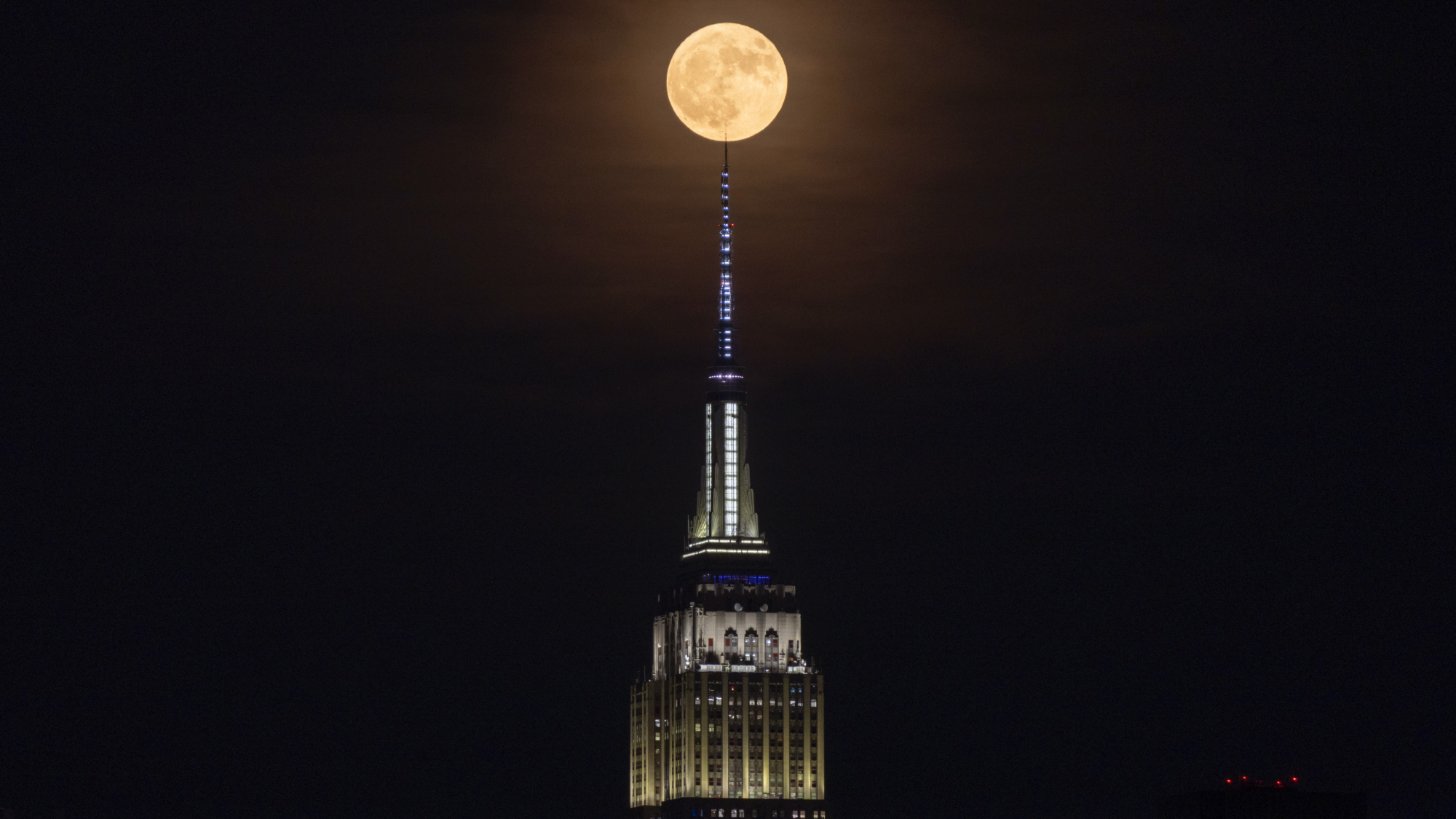 a fully illuminated moon appears at the very top of the Empire State Building.