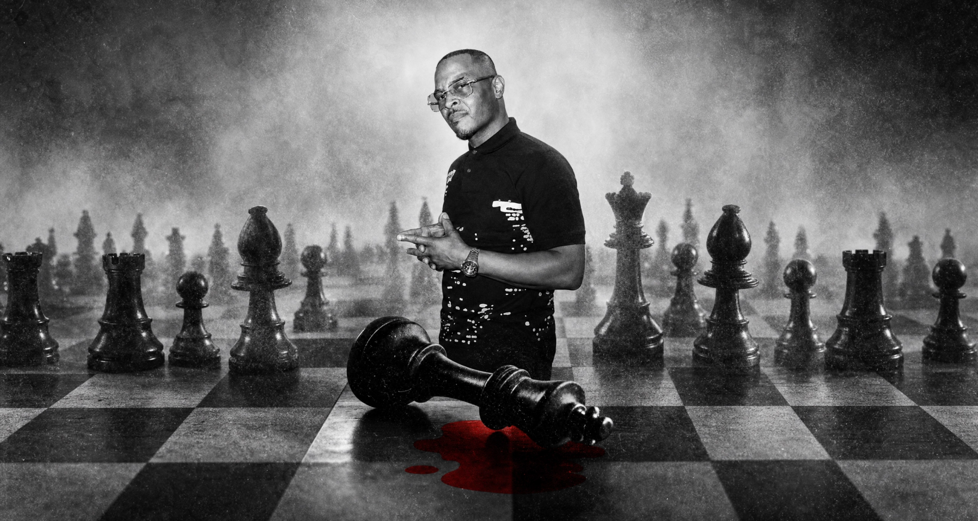 A man stands on a large chessboard with oversized pieces. A fallen king piece lies near him with a red stain beneath it.