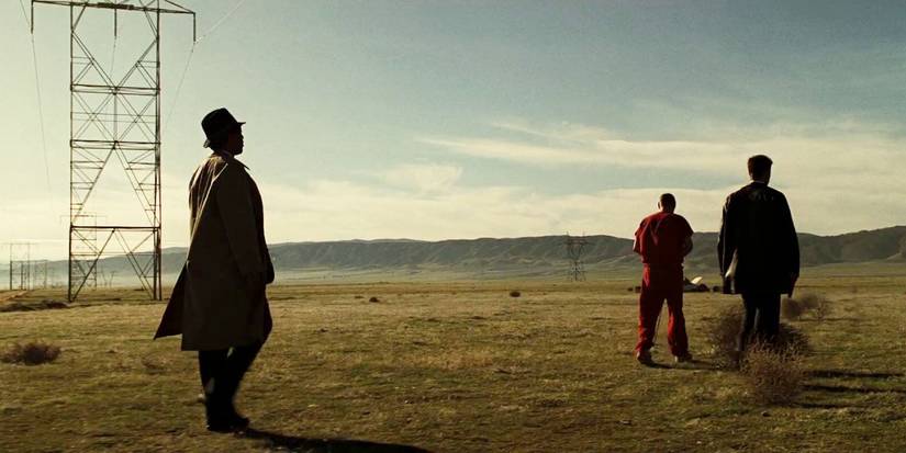 Two men guiding a prisoner across an open field in Se7en