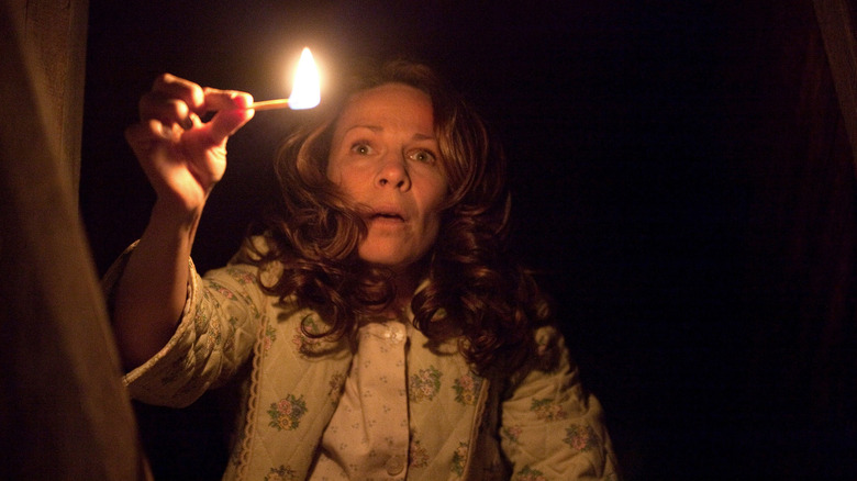 Lili Taylor as Carolyn Perron in The Conjuring, leaning over in the dark and lighting up her face with a match.