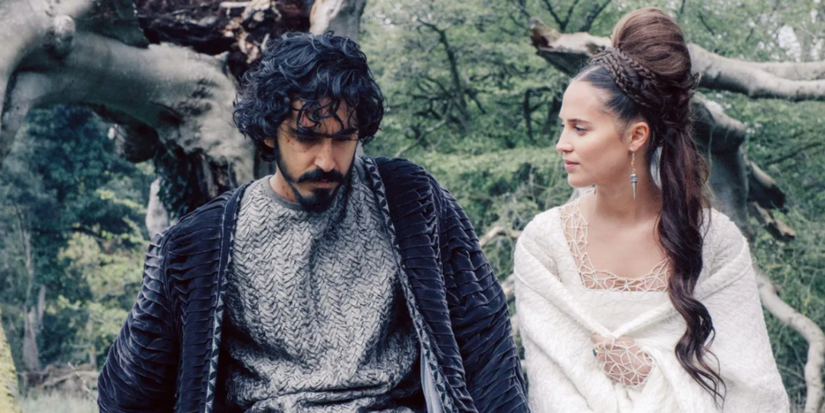 Dev Patel sits next to Alicia Vikander outside in 'The Green Knight'