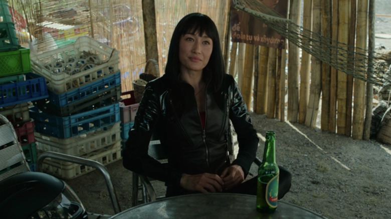 Maggie Q's Anna Dutton sits at a table with a beer in The Protégé