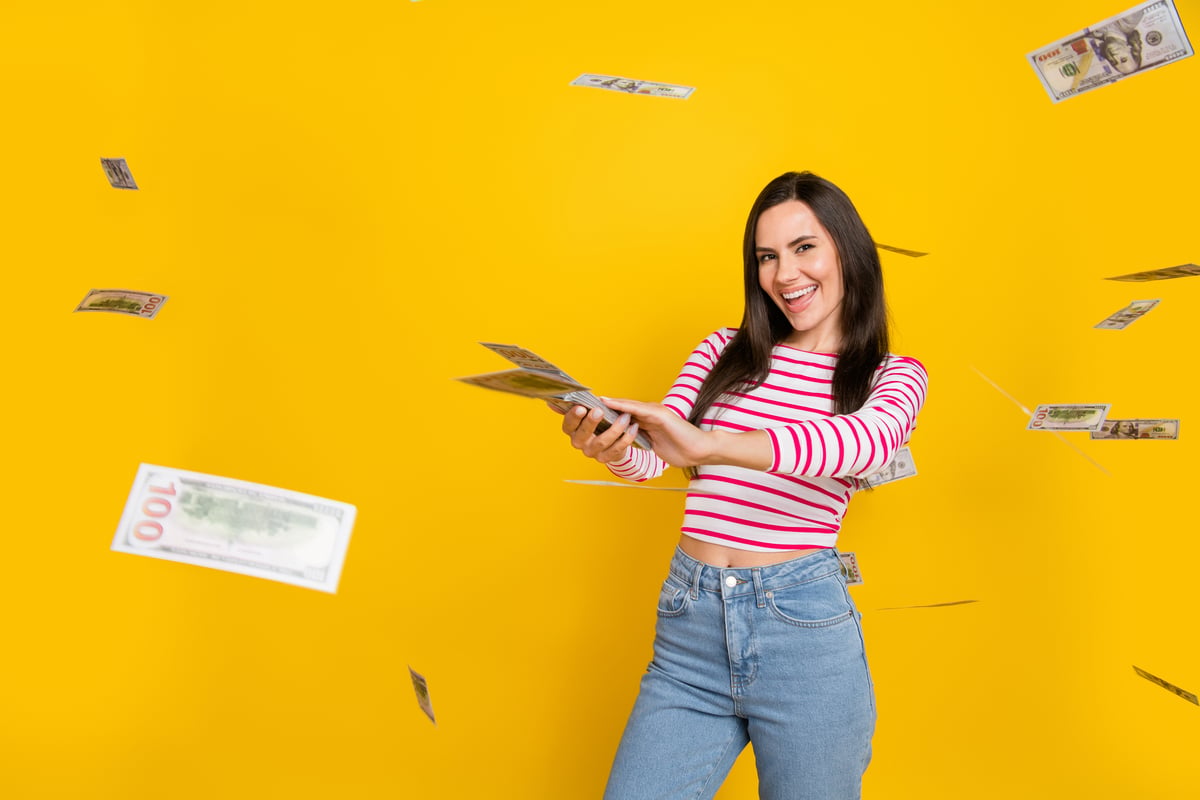 A person in a red-and-white striped shirt "makes it rain" with hundred-dollar bills against a yellow background.