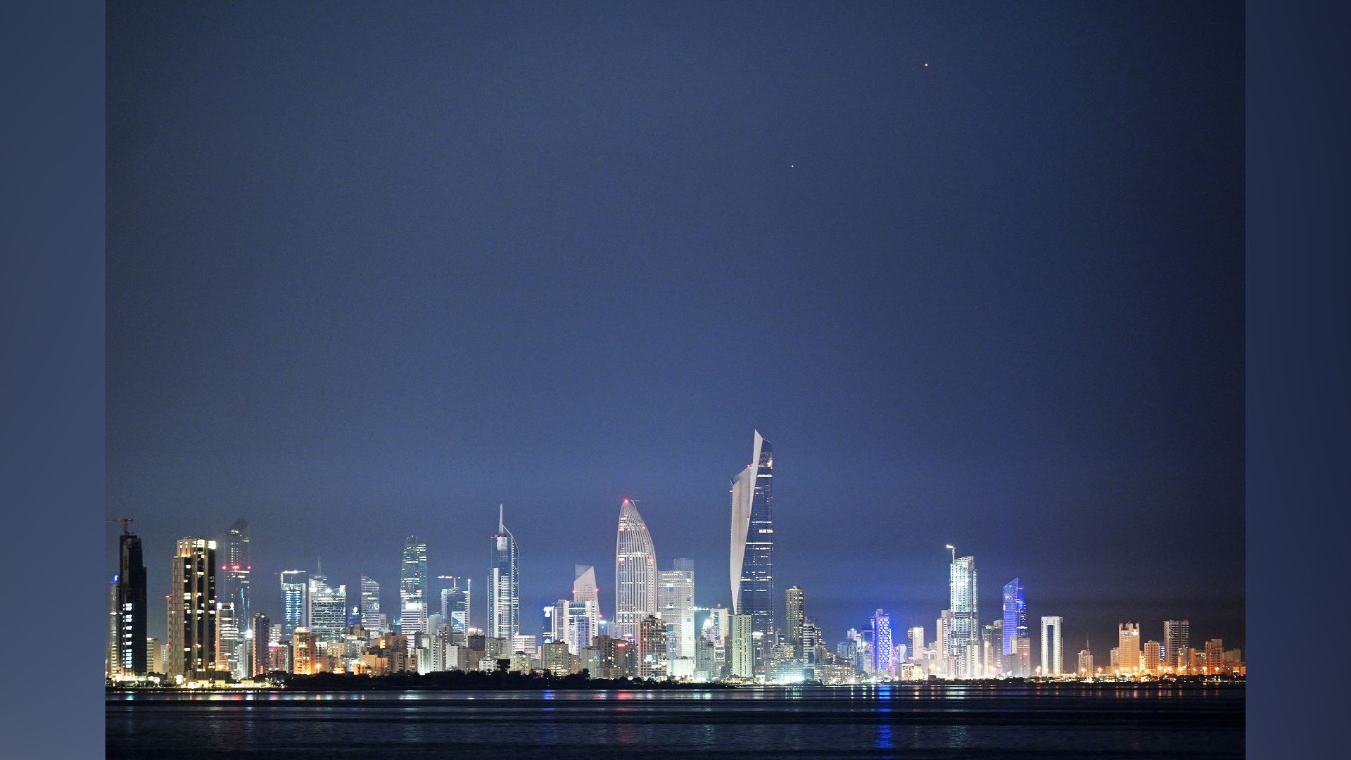 Two star-like planets glow close to one another in the night sky above a city skyline