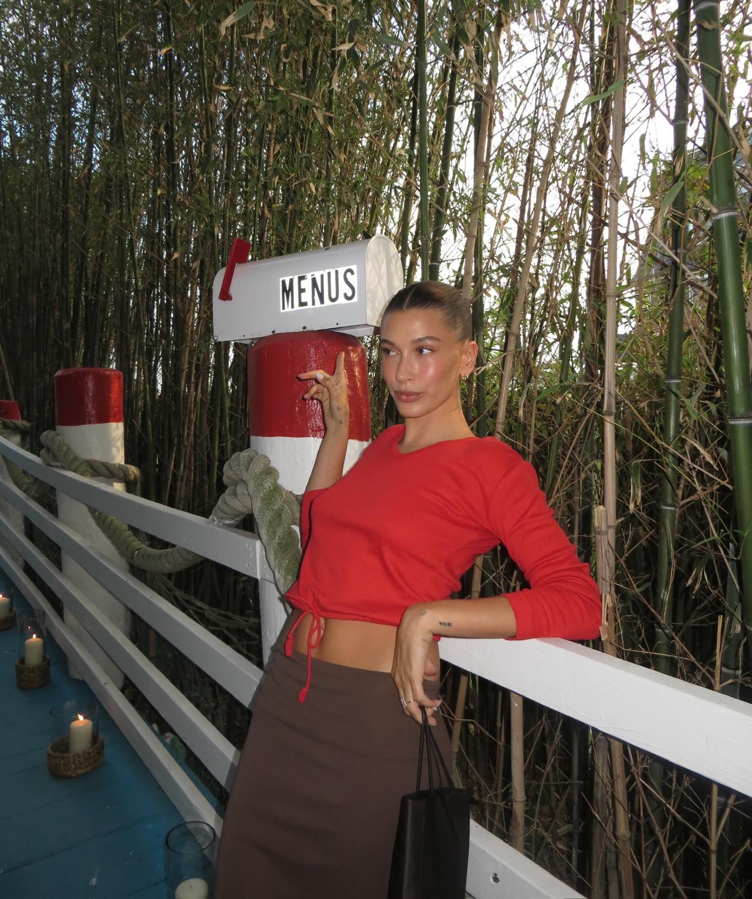 Hailey Bieber at her Rhode Island event wearing a red top and brown skirt with Staud thong sandals.