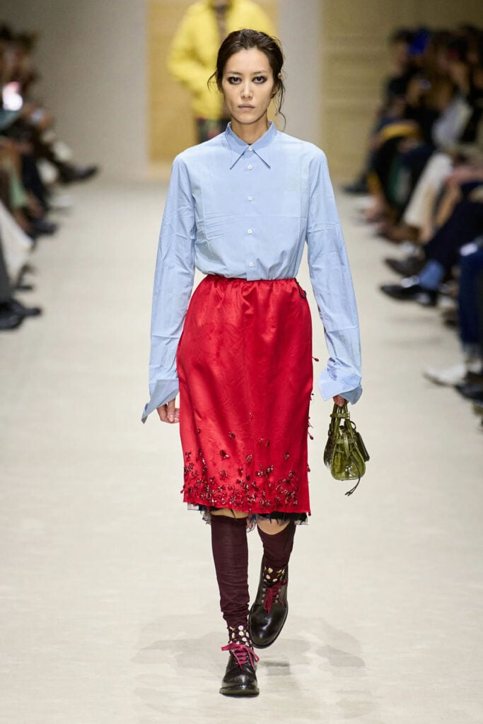 Prada Fall 2026 runway look featuring a pale blue shirt and embellished red skirt.