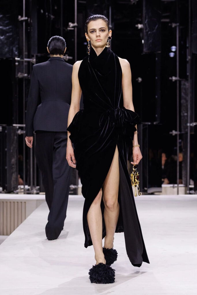 Model presents the Givenchy Fall 2026 black velvet gown with oversized bow-accented arm warmers on the runway.