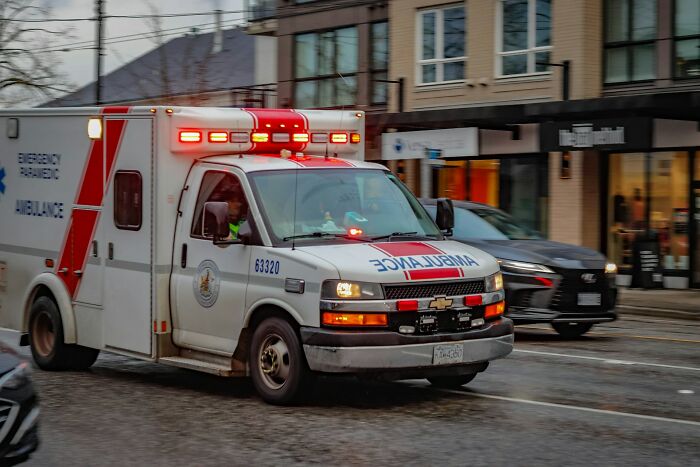 Ambulance with flashing lights driving on a city street, conveying what doctors do when a patient is faking it.