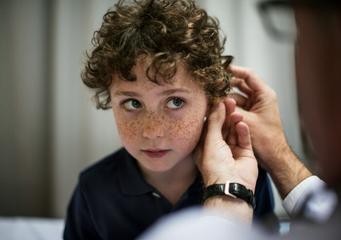 A young patient with freckles looks up while a doctor examines his ear, showing what doctors do when patients are faking.