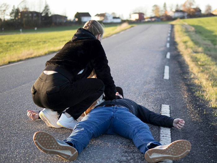 A person administering first aid to another person lying on a road, revealing a hidden side of hospitals.