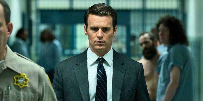 Jonathan Groff in a suit and tie walking through a prison in Mindhunter.