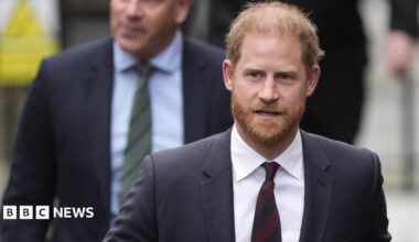 Prince Harry wearing a dark suit with a maroon tie.