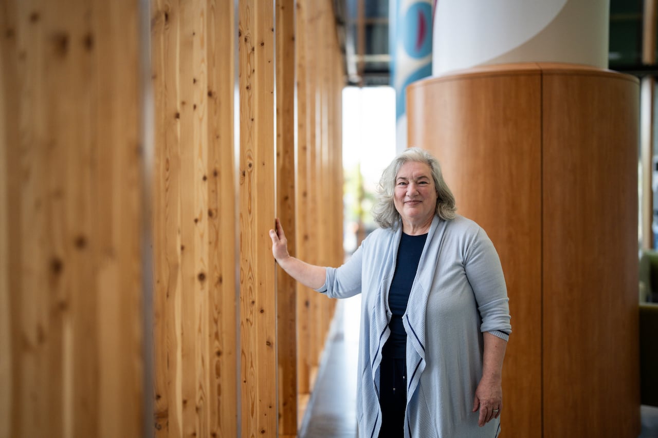 A woman posing for a photo puts one hand on a wooden beam.