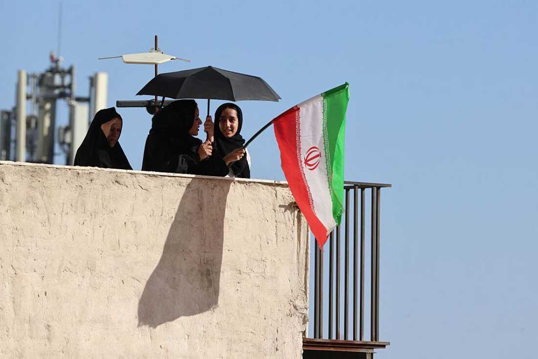 Mourners wave the Iranian flag on top of a building during the funeral procession for Iran's slain Supreme Leader Ali Khamenei and members of his family, before he is buried at the Shrine of Imam Reza, Iran's most revered place of worship, in Mashhad on July 9.