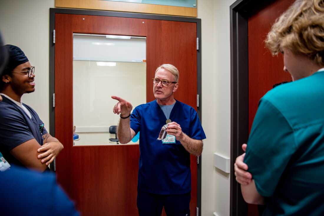 Adjunct instructor Steven Parsons instructs students on proper scrub technique during a clinical activity. He is wearing blue scrubs and three students are listening to him.