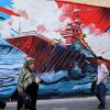 Commuters walk past a wall mural along the street in Tehran on July 21.