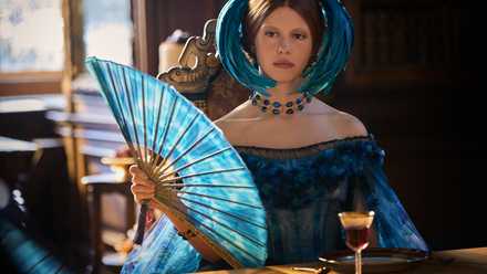 Mia Goth wearing a blue dress and holding a matching fan in Frankenstein