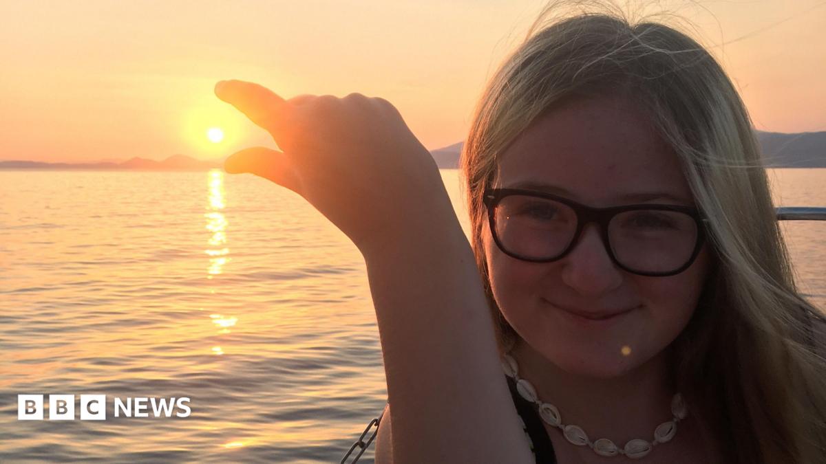 Lucy is wearing glasses and a necklace, posing as if she is trying to pinch the sun at sunset