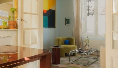 A living room with a lime-toned armchair, abstract colorful artwork, pale blue walls, a tubular chrome and glass coffee table, and white-washed wooden detailing.