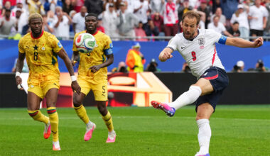 A soccer player kicks a ball in front of two other players in the background.