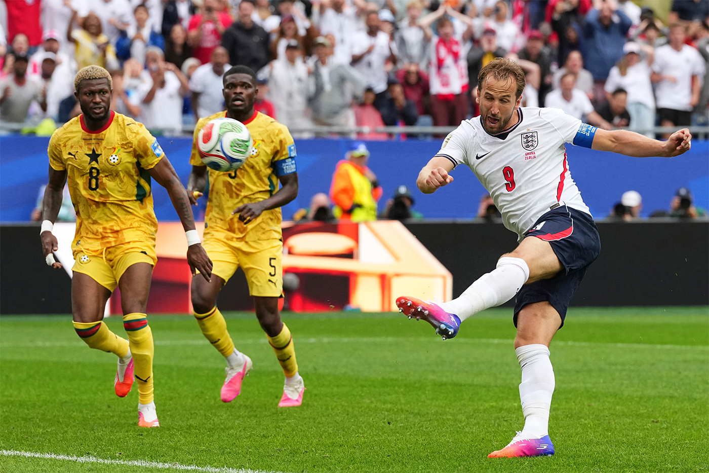A soccer player kicks a ball in front of two other players in the background.