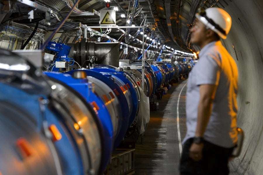 A man gazes at an instrument-festooned pipe that seems to stretch endlessly down a large tunnel.