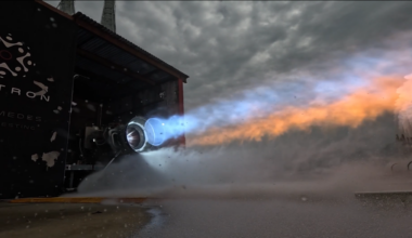 A rocket engine on a test stand blasts blue and orange flame.