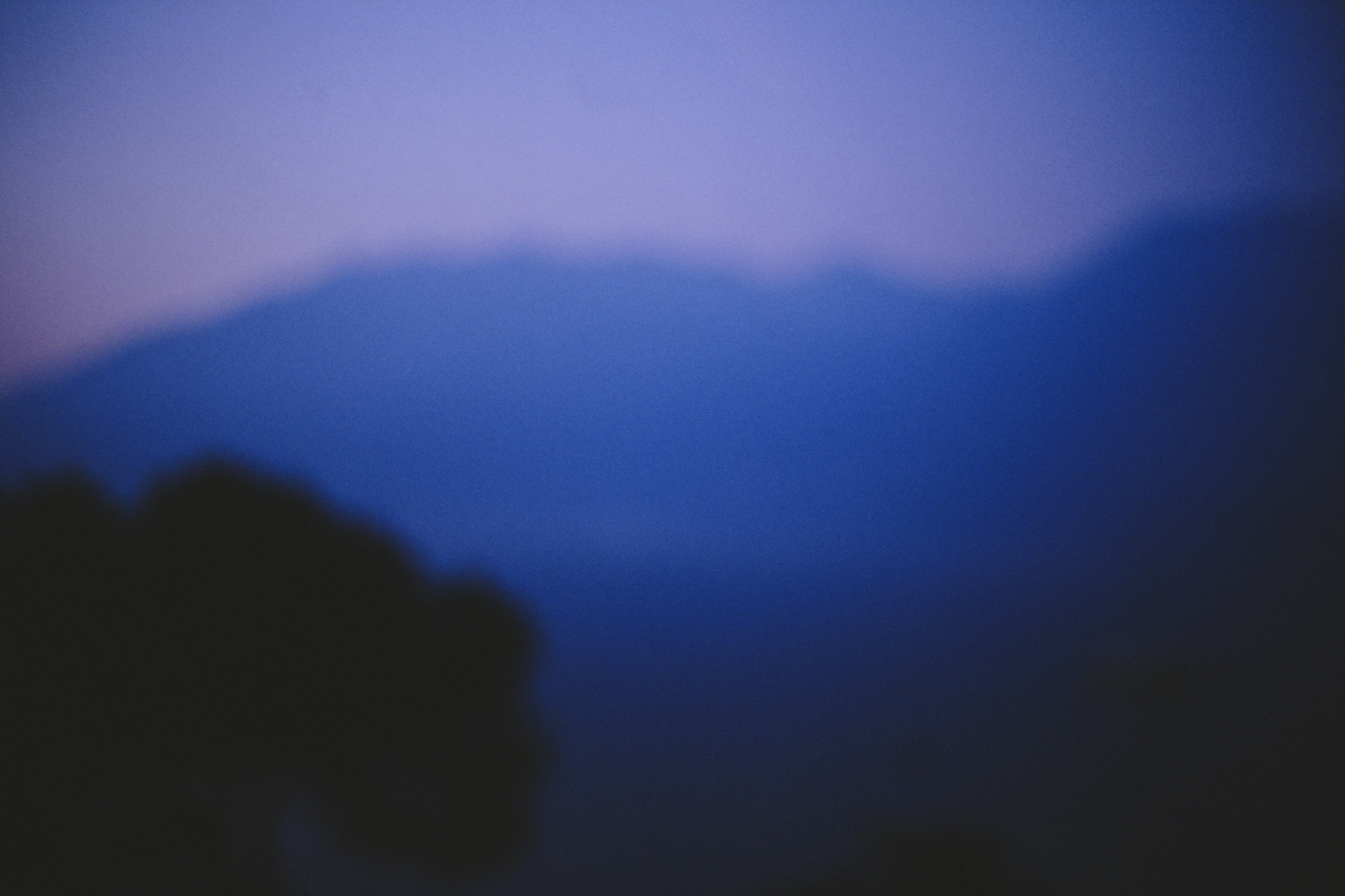 Rolling hills fade into deep blue dusk light beneath a hazy sky.