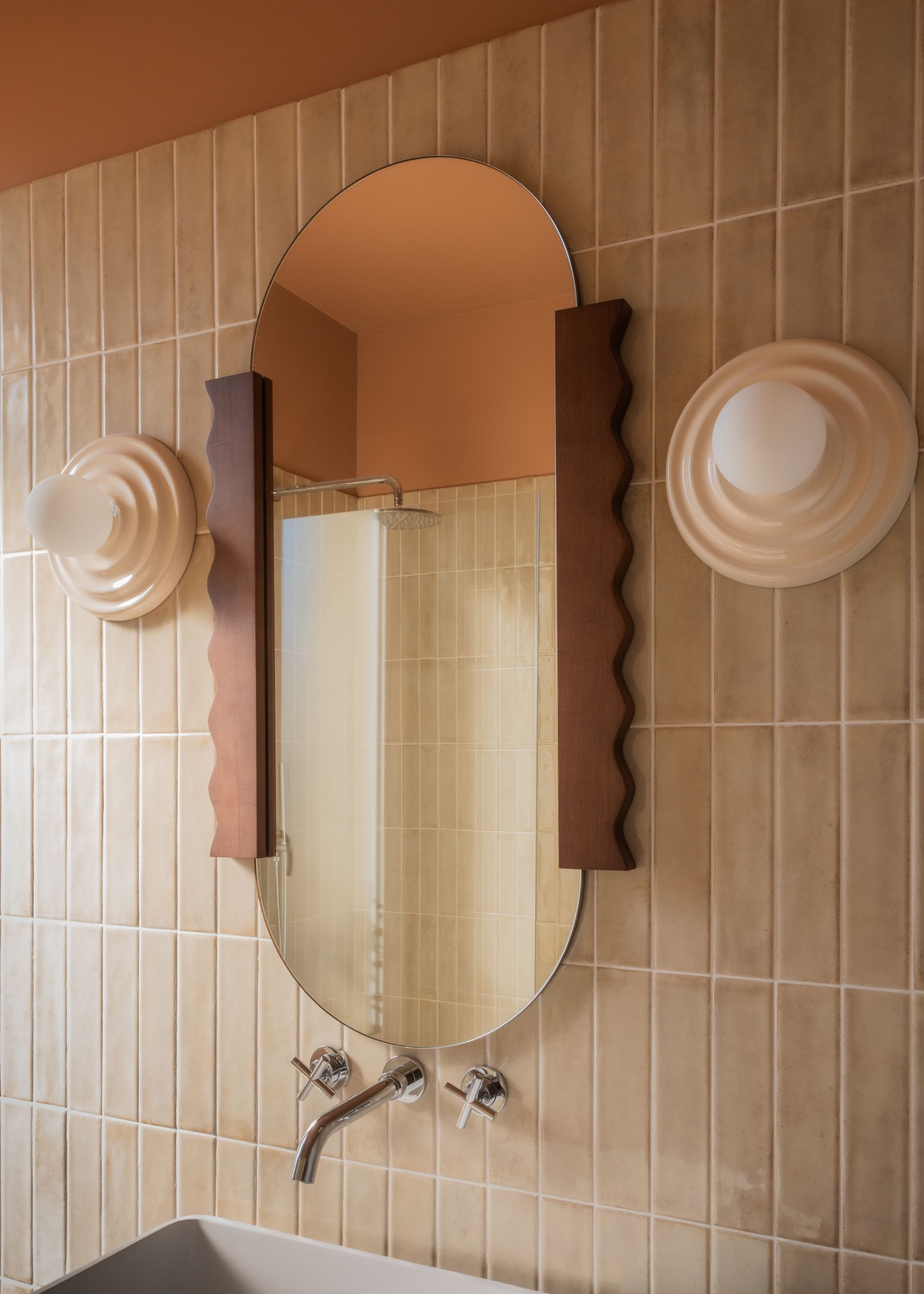 A bathroom with an oval mirror and pink wall lights