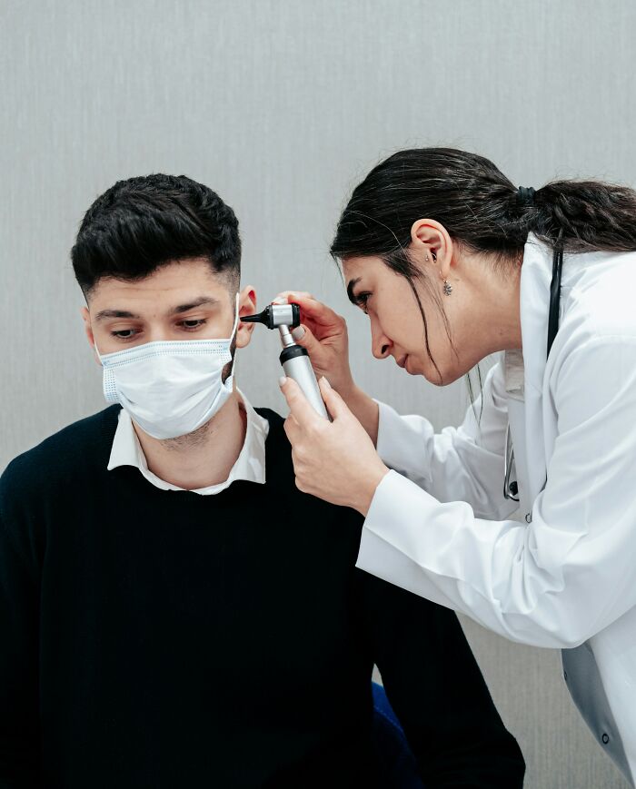 A doctor examining a patient's ear, mindful of situations where a patient is faking it.