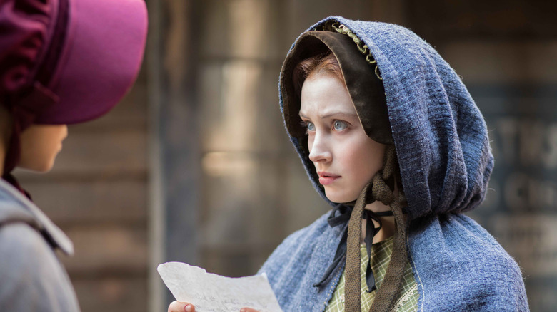 Sarah Gadon as Grace Marks wearing a blue hooded cloak and holding a piece of paper in Alias Grace.