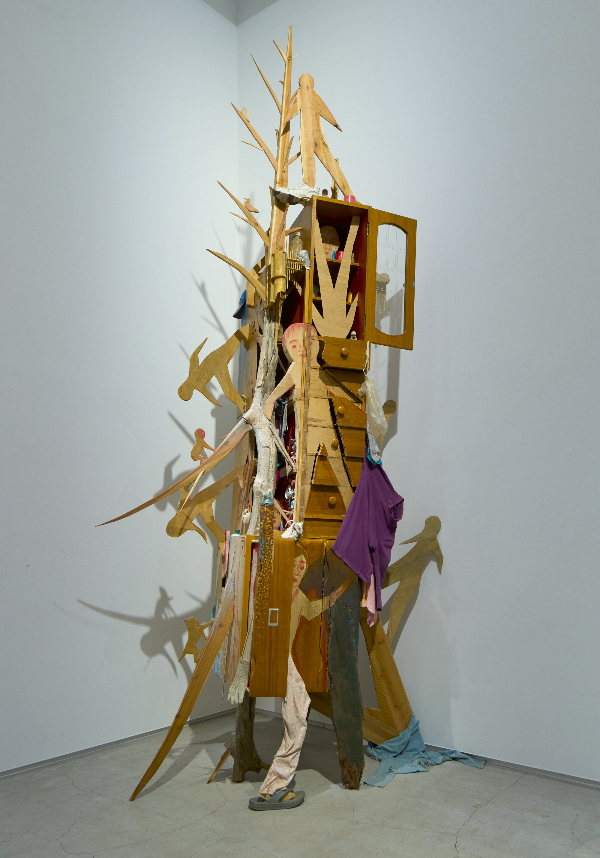 a wooden assemblage sculpture by Fumiaki Aono of figures scaling a towering piece of furniture