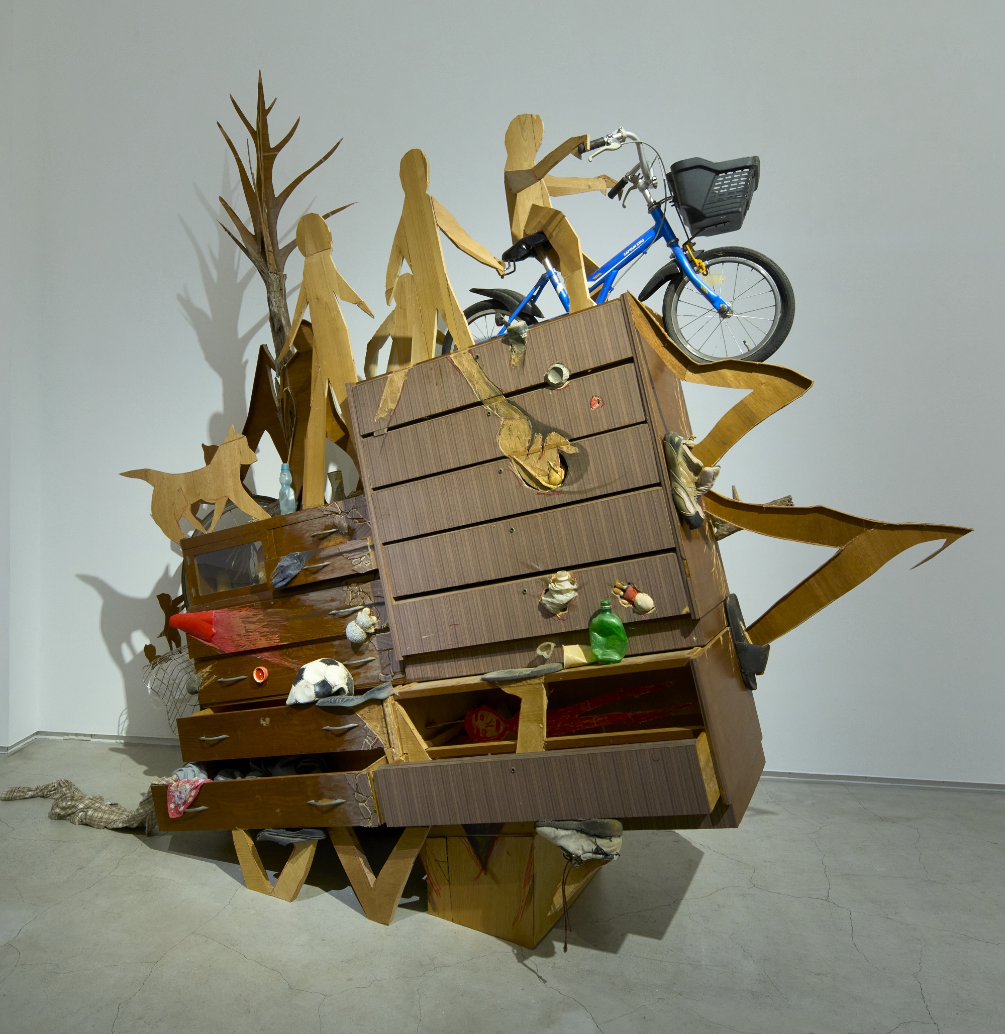 a wooden assemblage sculpture by Fumiaki Aono of figures, trees, and a dog
