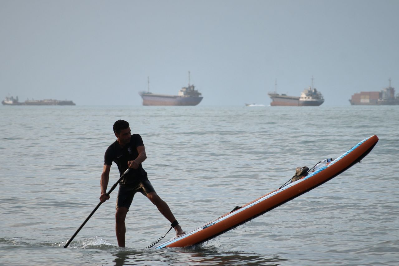 A man paddles a stand-up paddleboard, as cargo ships and other commercial vessels appear anchored in the Strait of Hormuz off Bandar Abbas, Iran, on Monday.