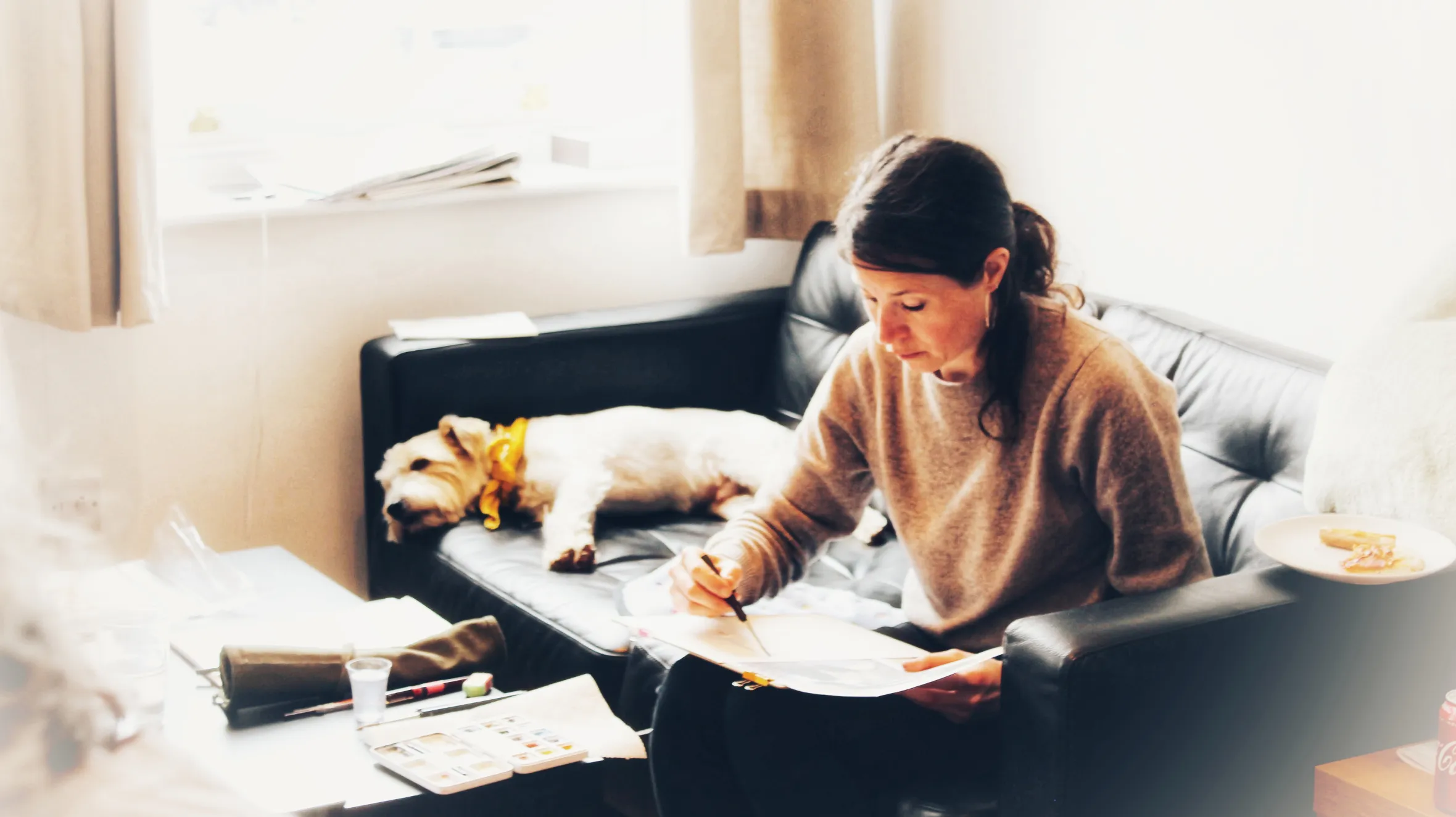 Artist Alice Hawthorn drawing on a sofa with her dog.