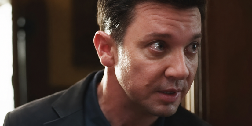 Jeremy Renner looking wide-eyed and anxious inside a dimly lit room in a scene from Wake Up Dead Man: A Knives Out Mystery.