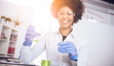 A medical researcher in a white coat holds laboratory equipment and smiles.