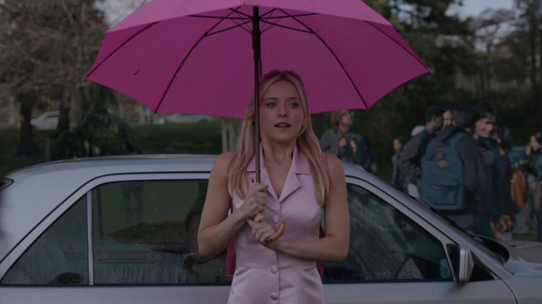 Elle in a pink outfit, carrying a pink umbrella as she exits a car