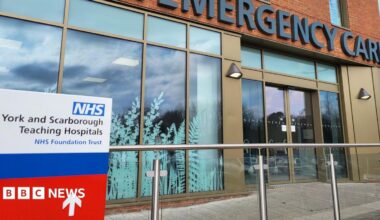The exterior of a hospital building, with large glass windows and doors, and a sign that reads York and Scarborough Teaching Hospitals.