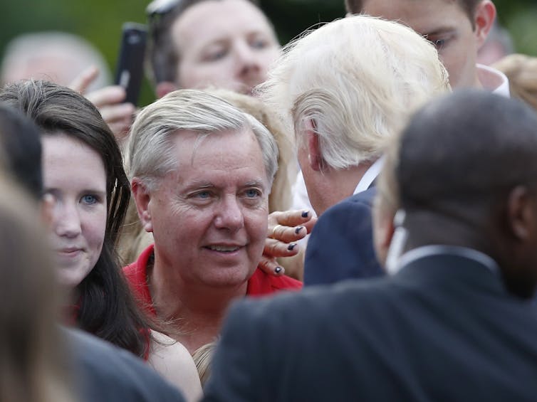 A man in a red shirt looks at another man in a suit and tie.