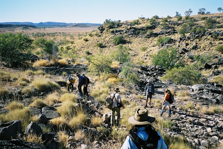 A group of people walking through rocky shrub.