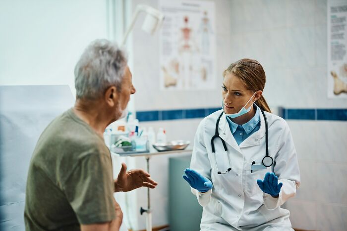 Female doctor in scrubs and mask talking to a male patient, illustrating what doctors do when a patient is faking it.