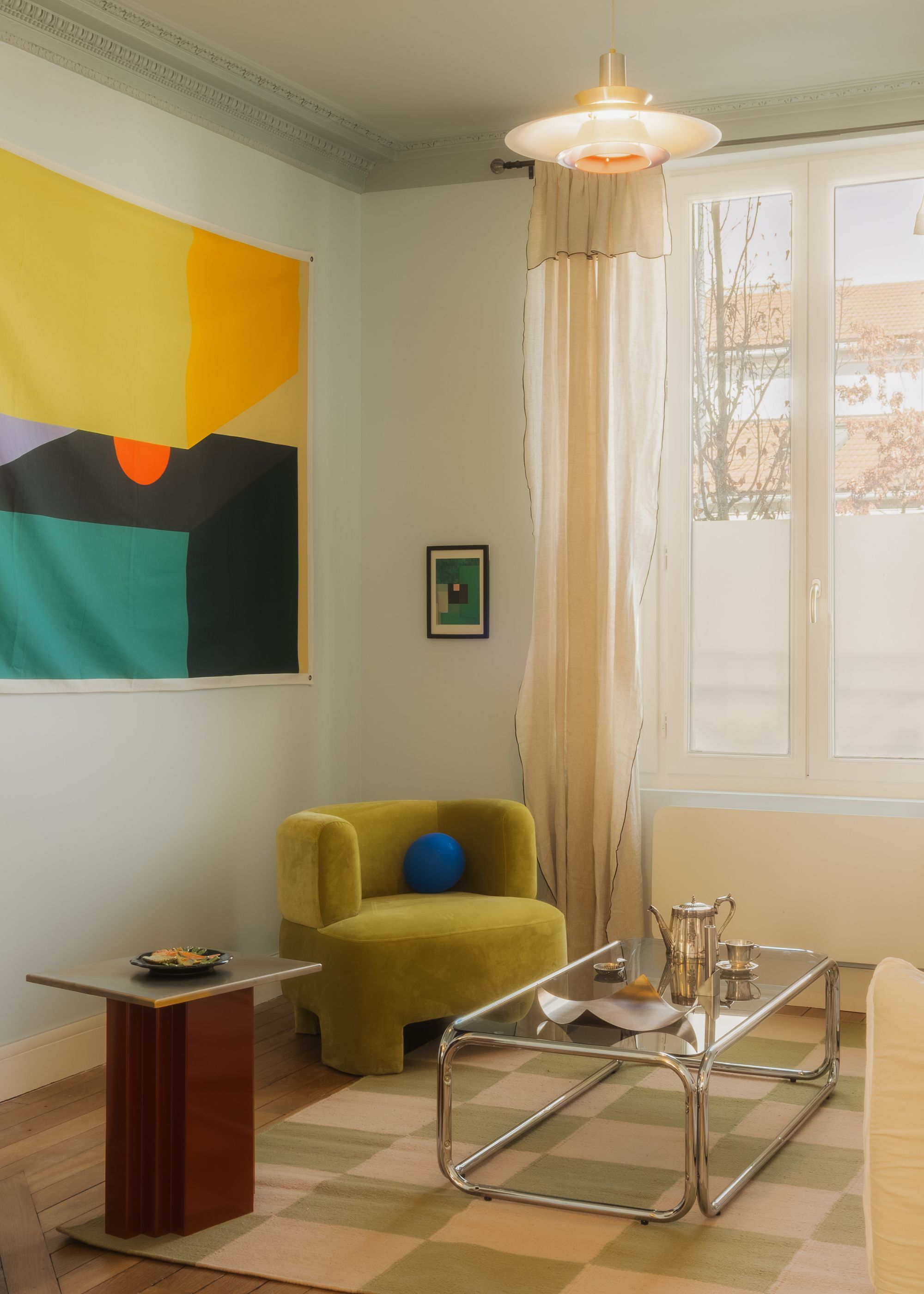 A living room with green armchair, a multicolored artwork, carpet and glass coffee table
