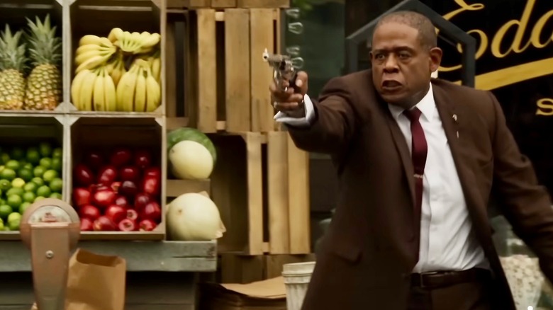 Bumpy Johnson walking and pointing a gun by a fruit stand outside