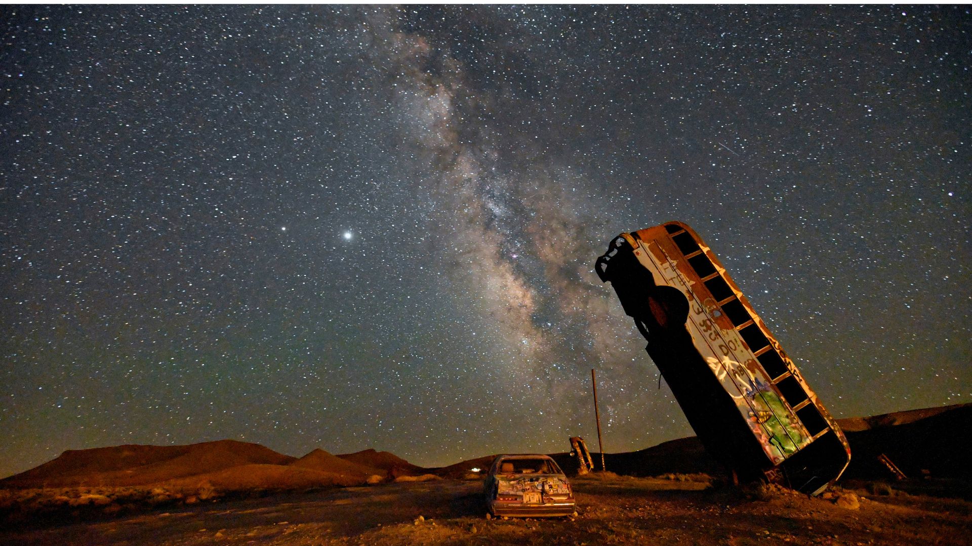 A bus is photographed balanced on its end in the desert as the Milky Way arches overhead at night
