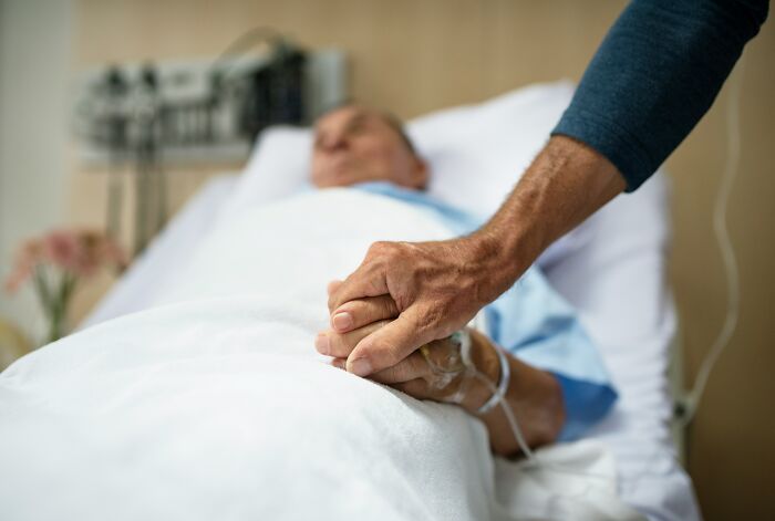 A hand holding another patient's hand with an IV drip, illustrating hospital horror stories.