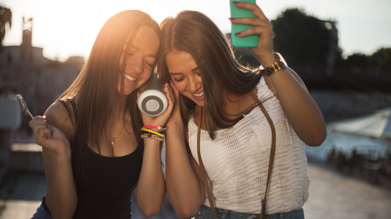 Two girls listening to music from a speaker, under the summer sun.