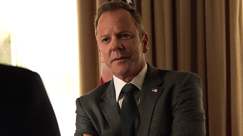 President Tom Kirkman in a gray suit standing with his arms crossed in front of tan curtains in Designated Survivor
